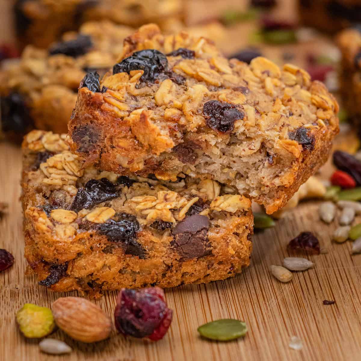 Baked oatmeal squares with dried fruit, nuts, and chocolate chips on a wooden cutting board.