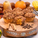 Cinnamon streusel pumpkin muffins rest atop a wooden platform. Key ingredients and fall decor surround the delicious treats.