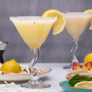 Two martini glasses are on display. They are filled with lemon drop cocktails. Key ingredients surround the celebratory drink.